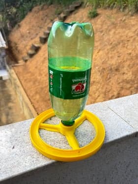 Foto de um bebedouro amarelo impresso em 3D, com uma garrafa PET rosqueada na base